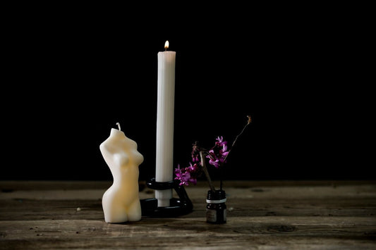a white candle and a black candle holder on a wooden table